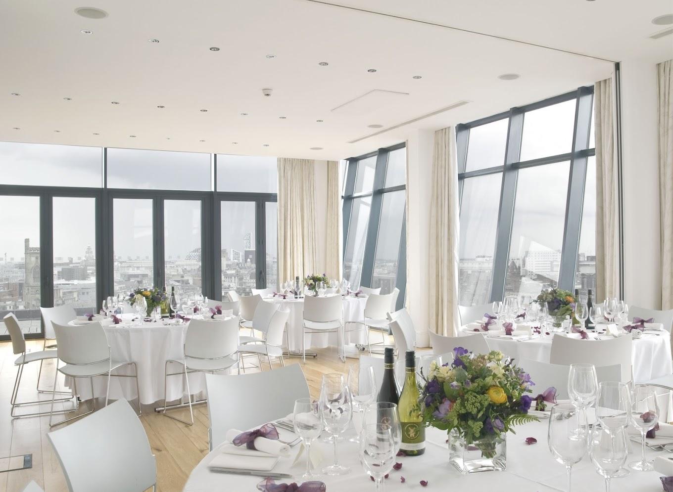 A function room with floor-to-ceiling windows, round tables with white linens, and city views at Hope Street Hotel.