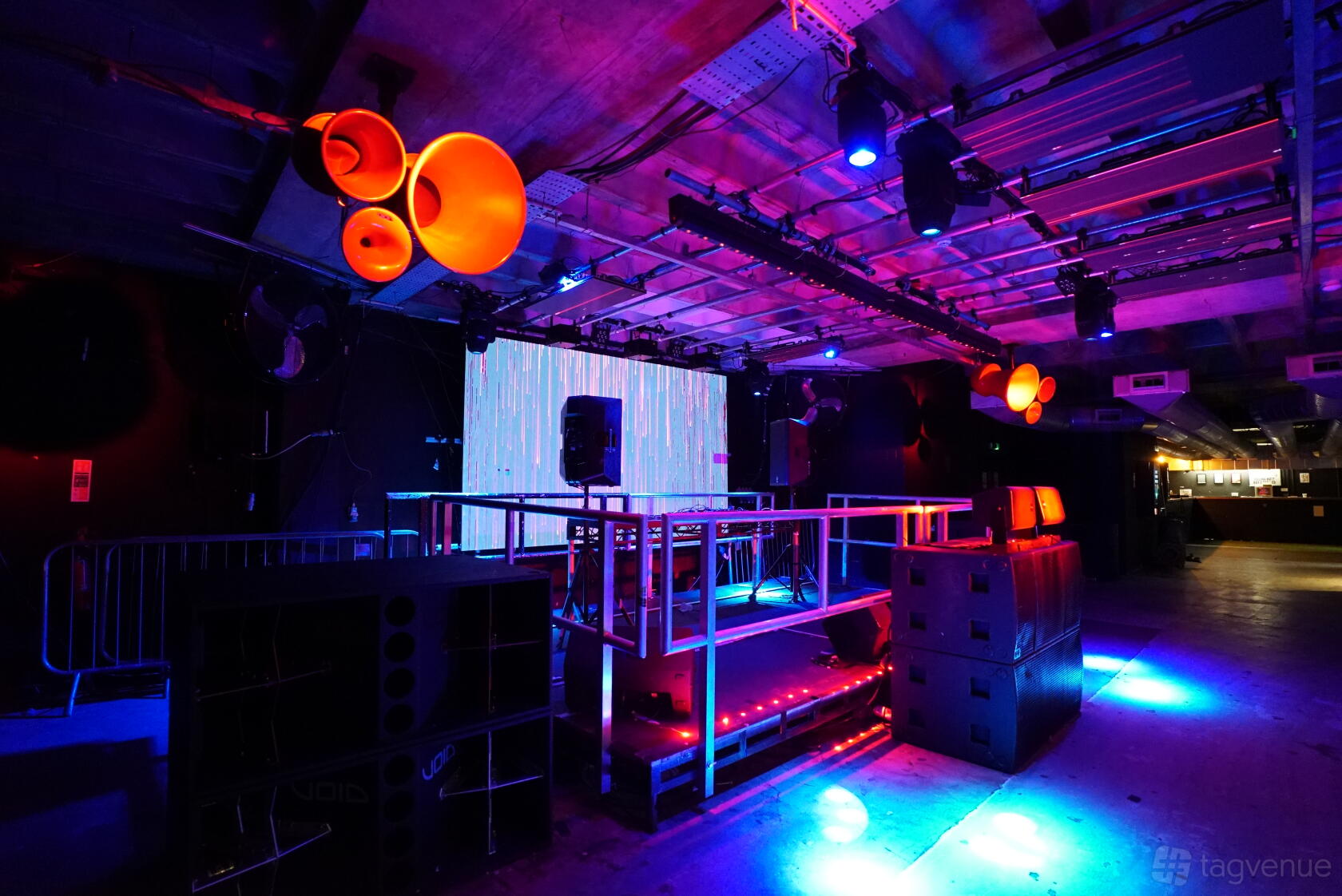 An event venue with a raised DJ booth, stage lighting, and industrial ceiling fixtures at Clock Factory.