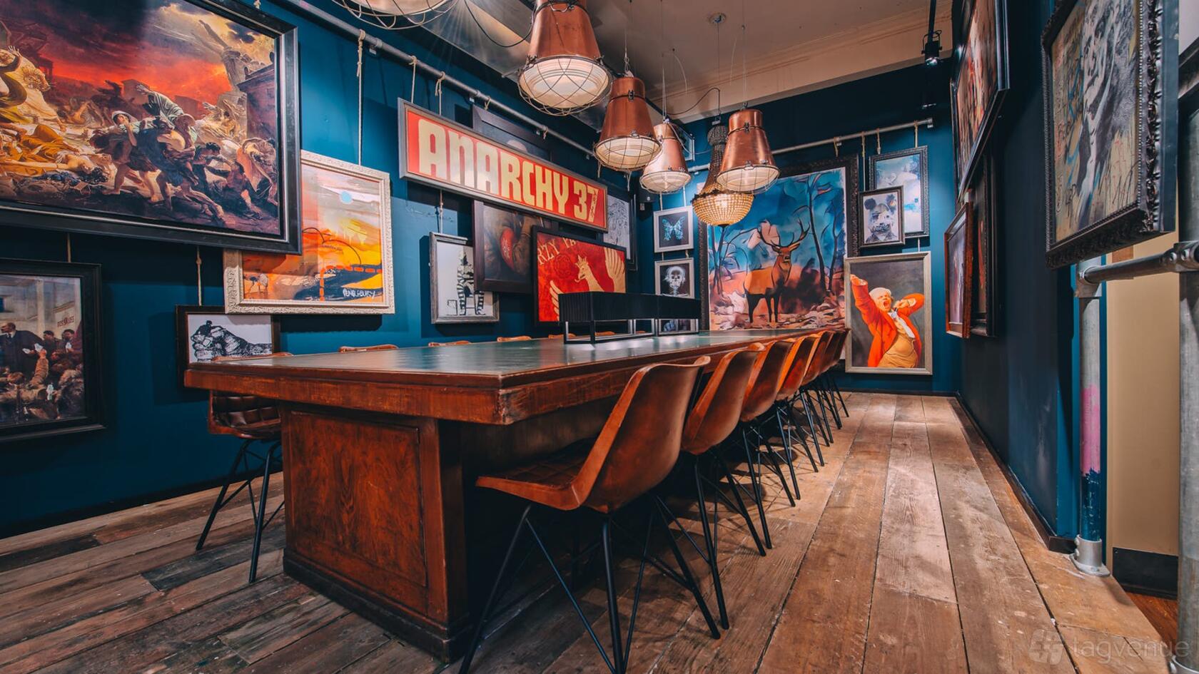 An event space in a bar with a long wooden table, leather chairs, and eclectic framed artwork at Revolution Mitchell Street.