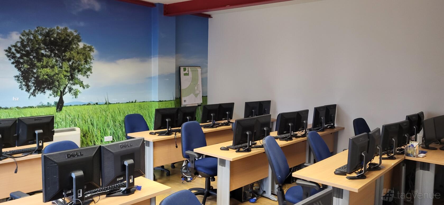 A training room with rows of computer workstations, blue chairs, and a mural of a green field at Nexus Human Training Centre.