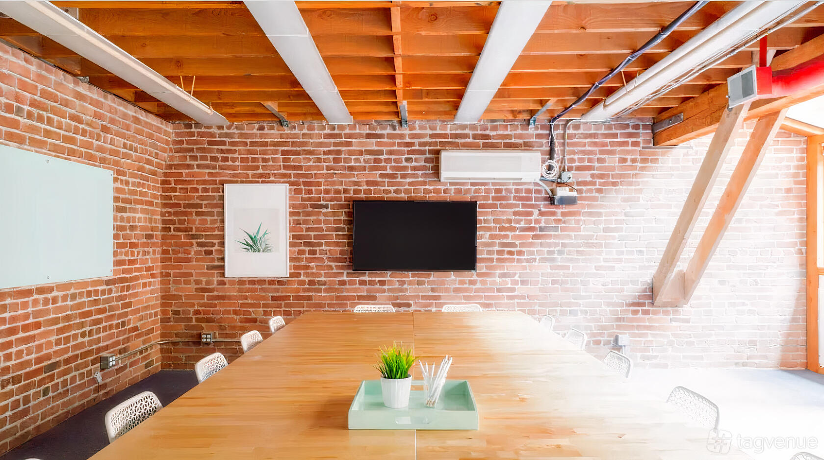 A meeting room with exposed brick walls, wooden beam ceiling, and a long conference table at 350 Townsend.