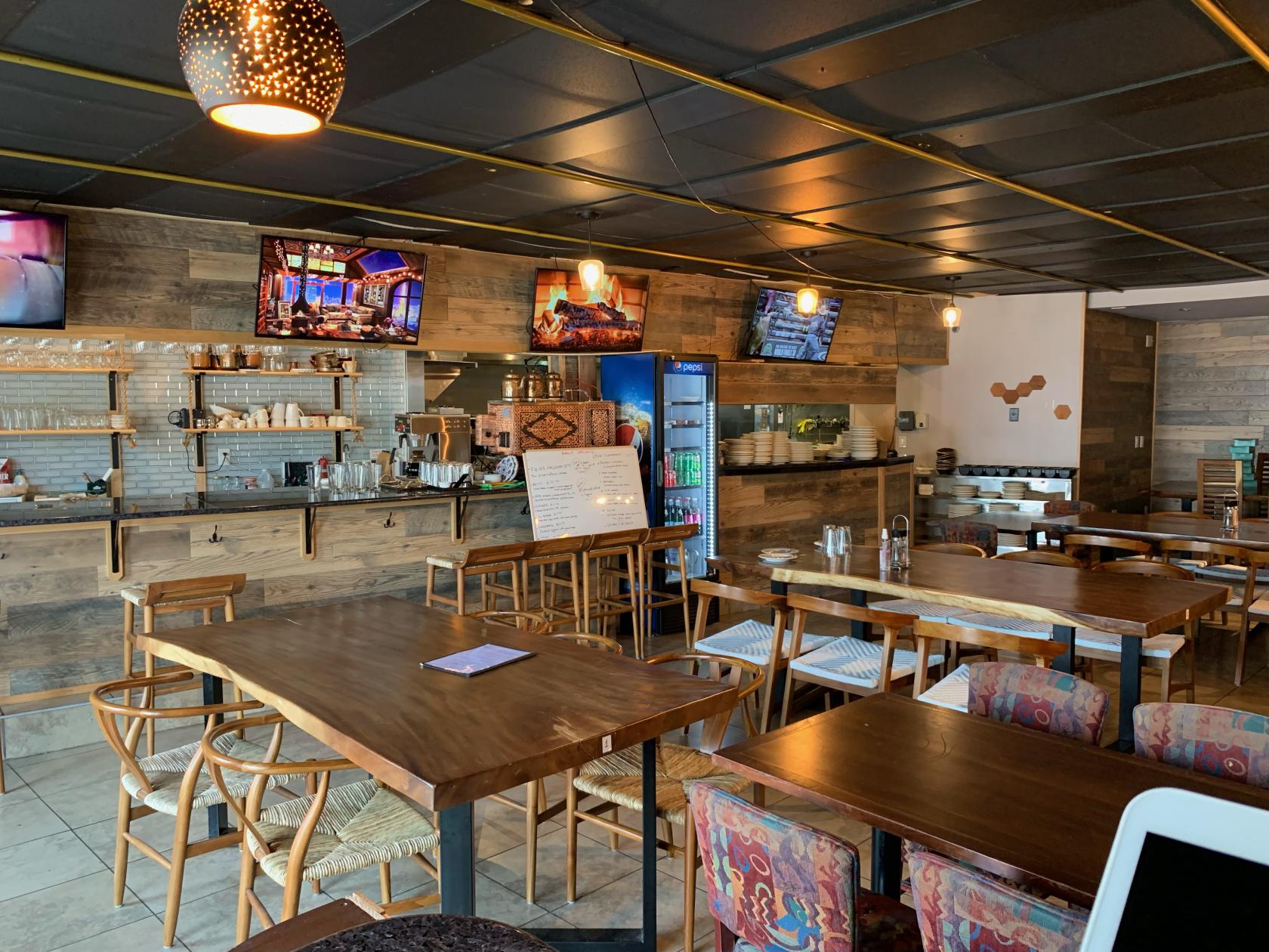 A bar with wooden tables, open shelving behind the counter, and overhead pendant lighting at Lavash Bar & Grille.