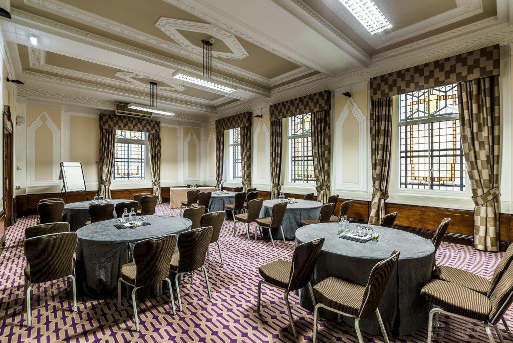 A conference centre room with round tables, patterned carpeting, and large windows with patterned drapes at Grand Connaught Rooms.