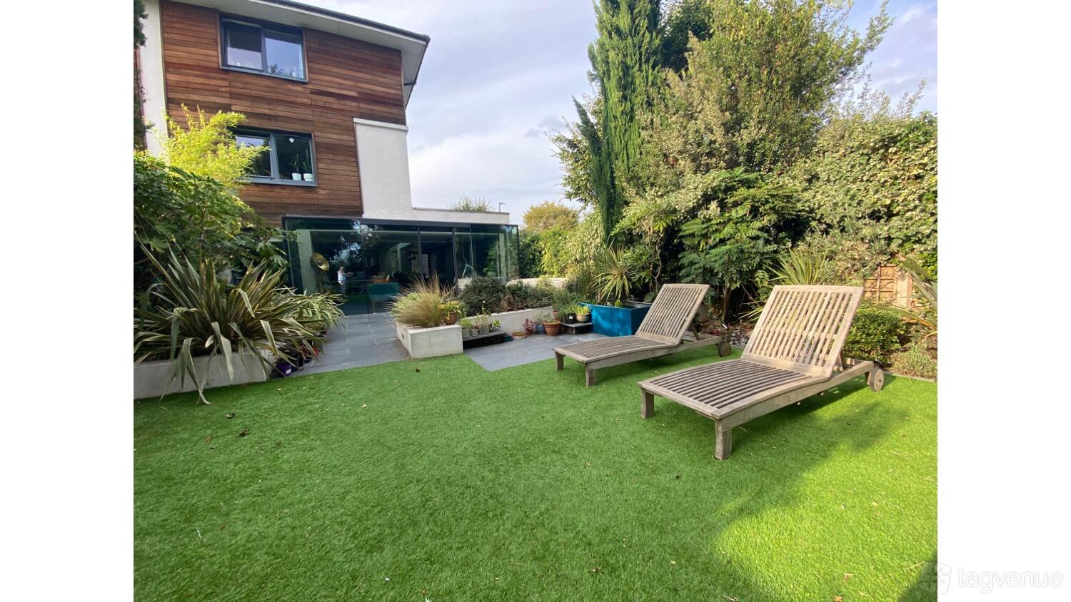 A house with a landscaped garden, artificial turf, greenery, and wooden lounge chairs at Whitelands Crescent.