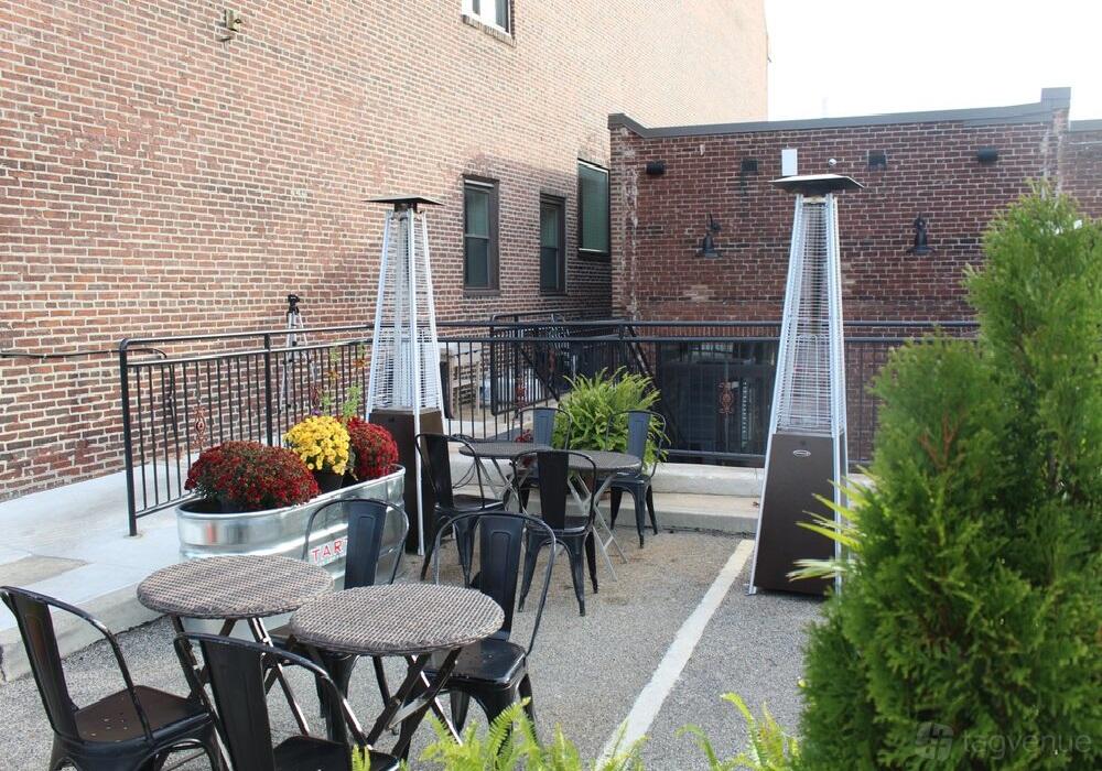 An outdoor restaurant patio with round tables, metal chairs, tall patio heaters, and potted plants at Newbolds Food & Libations.