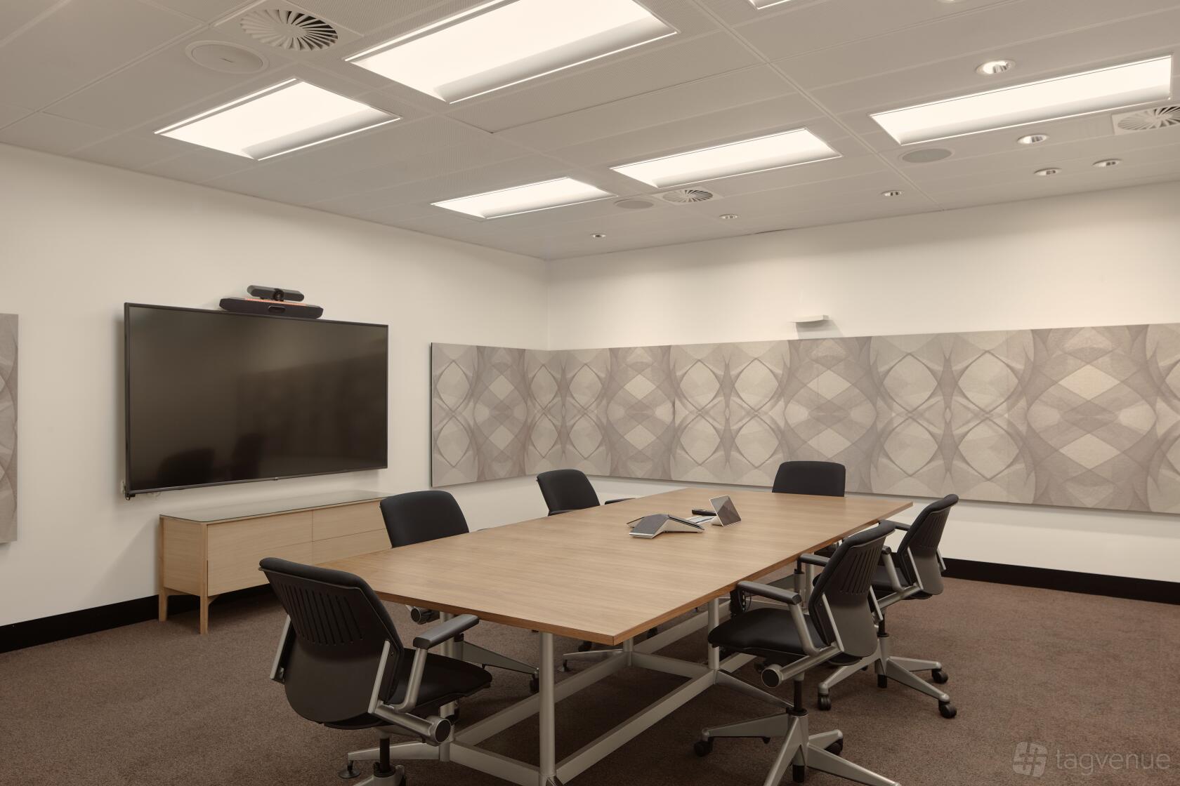 A meeting room with a rectangular wooden table, black chairs, large wall-mounted screen, and acoustic panels at Flex by ISPT at 4 National Circuit.