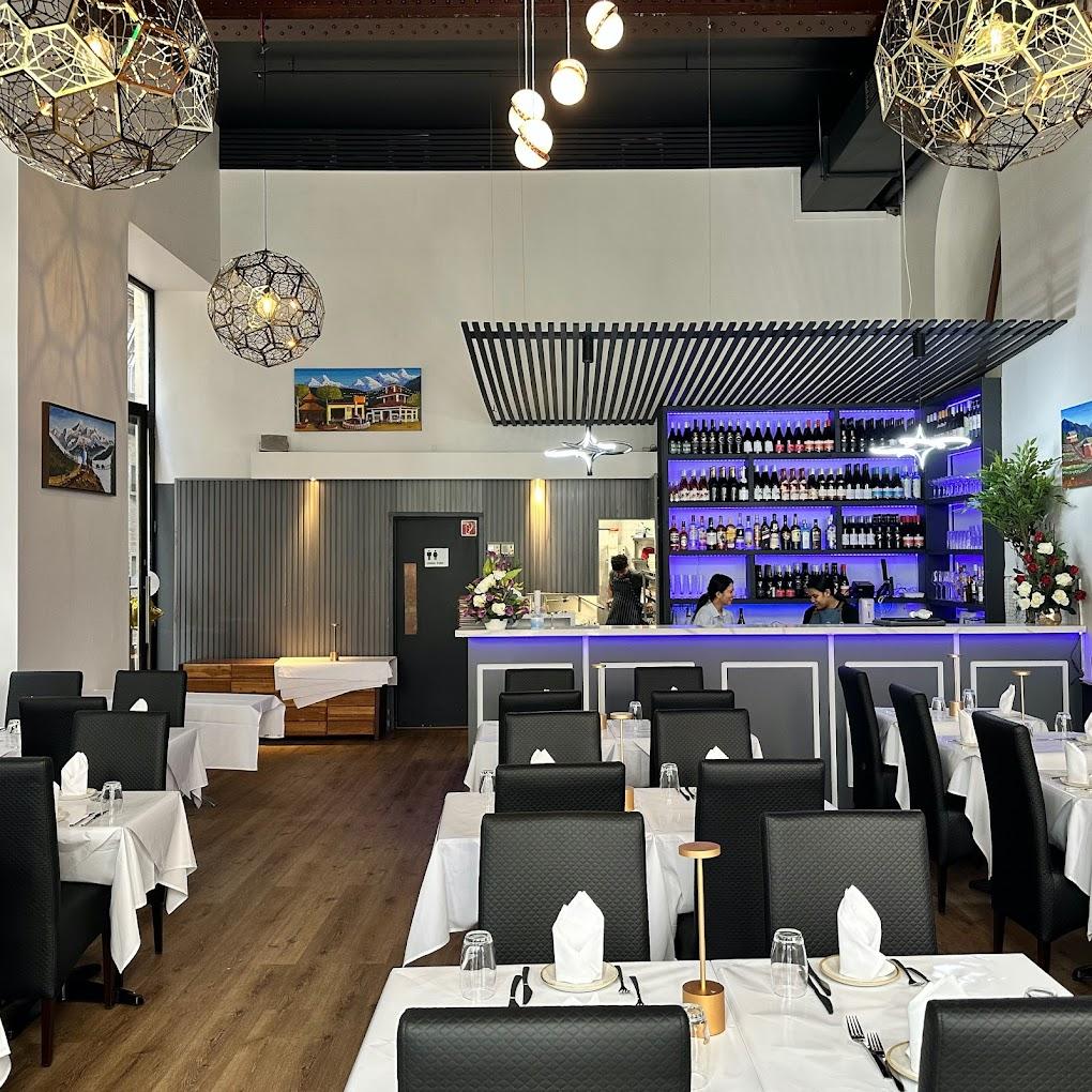 A restaurant with a backlit bar display, black chairs, and white tablecloths at AAGAMAN – PORT MELBOURNE.