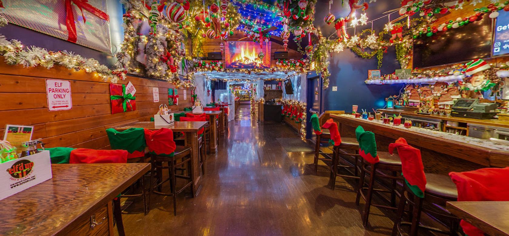 A festive bar with holiday decorations, garlands, string lights, and wrapped gifts on tables at Elf’d Up.