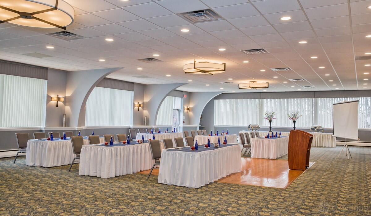 A ballroom with large windows, round chandeliers, and banquet tables draped in white linens at Kenilworth Inn.