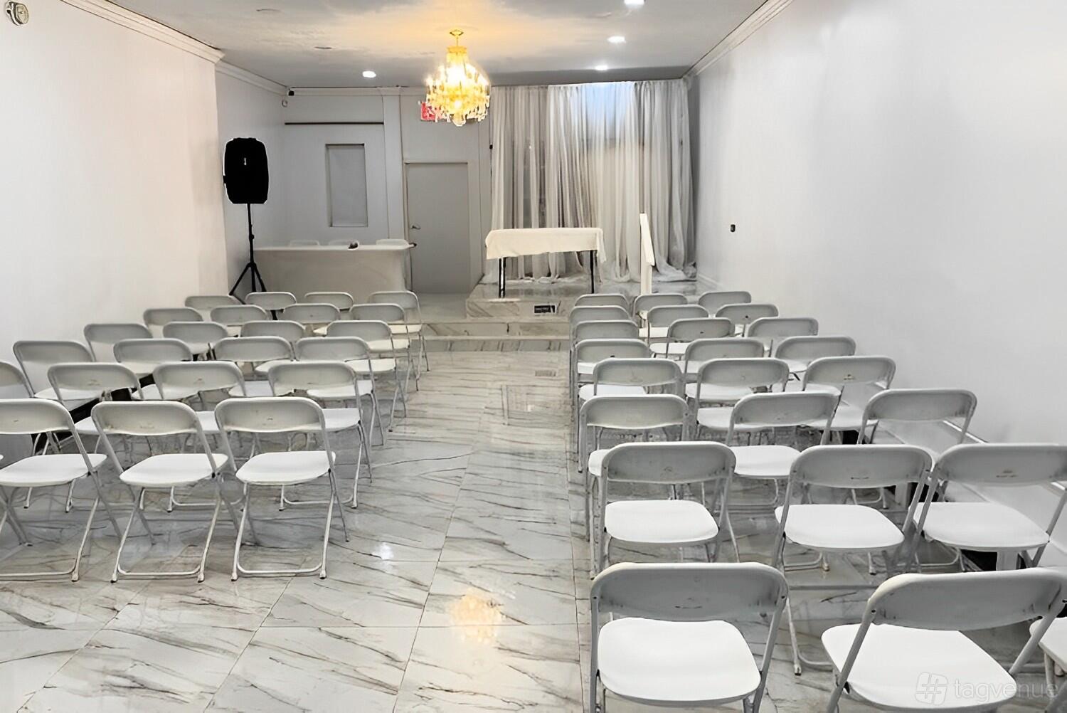 A hall with marble flooring, rows of white folding chairs, and a chandelier at Vaughn's Venue.