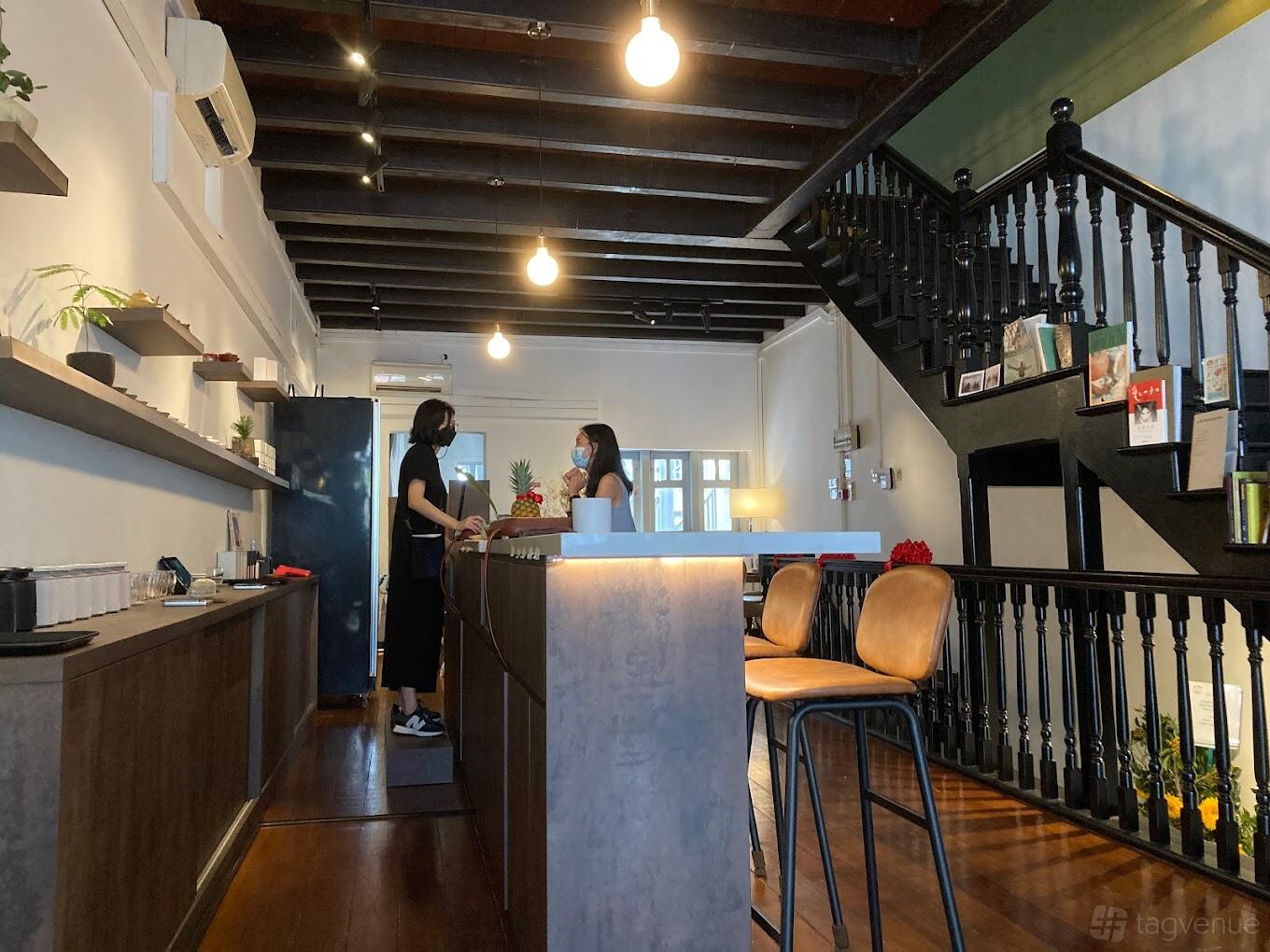 A cafe with exposed beam ceiling, pendant lights, a concrete counter, and wooden staircase at SILK Tea Bar.