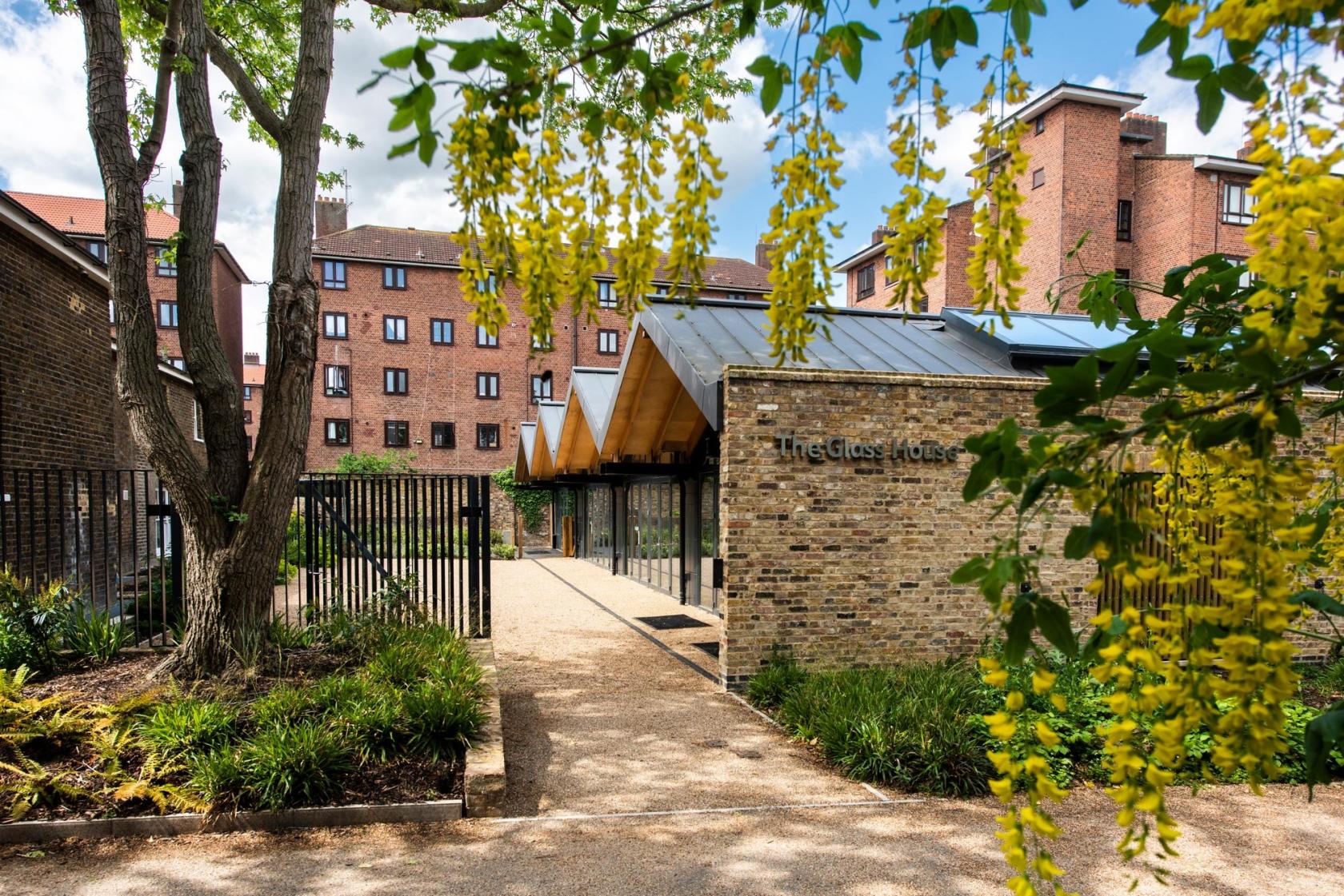 A versatile event space with floor-to-ceiling windows, brick exterior walls, and landscaped paths at The Glass House - Springfield Park.