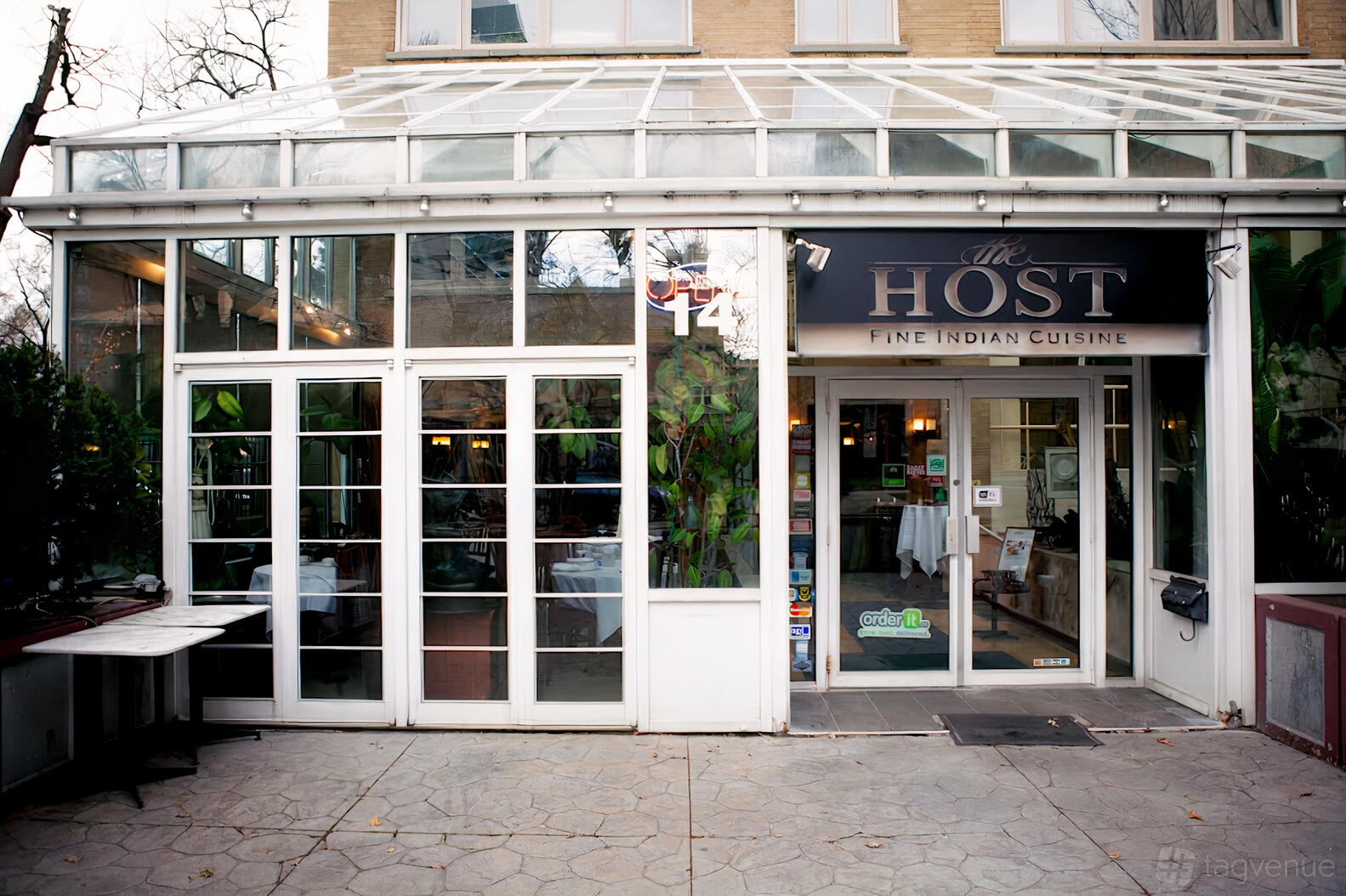A restaurant entrance with glass doors, large windows, and visible greenery at The Host.