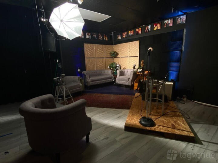 A studio with a small stage, microphone stand, soft lighting, and gray armchairs at LA School of Comedy.