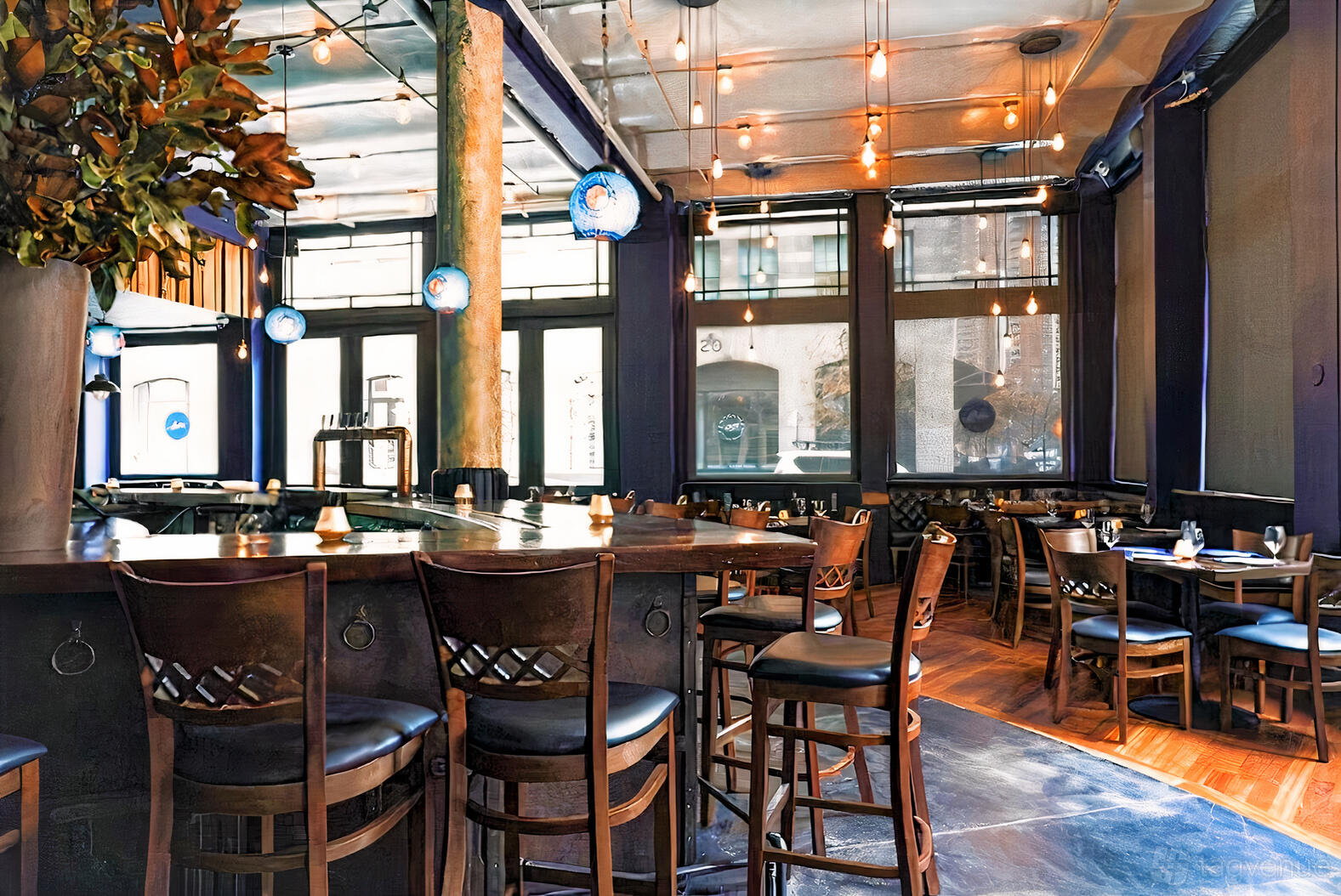 A restaurant with floor-to-ceiling windows, pendant lighting, and wooden tables with matching chairs at Paisley.