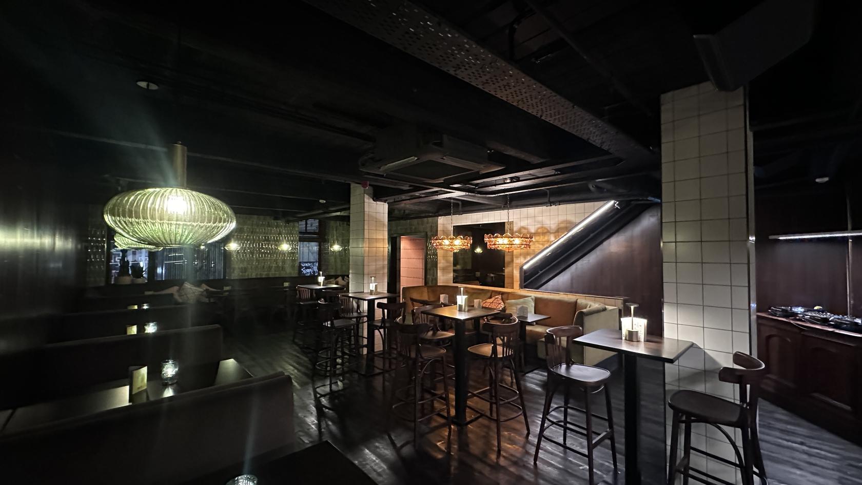 An event space with dark wood floors, ambient pendant lighting, and a mix of bar stools and booths at Boogalú.