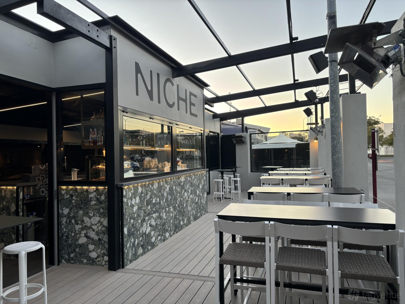 An outdoor bar area with high tables, white chairs, and a marble-fronted counter at Niche Bar.