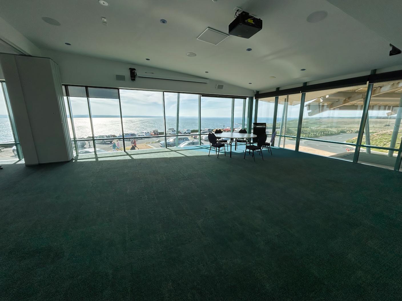 An event venue with floor-to-ceiling windows, green carpet, and ocean views at Nobbies Centre.