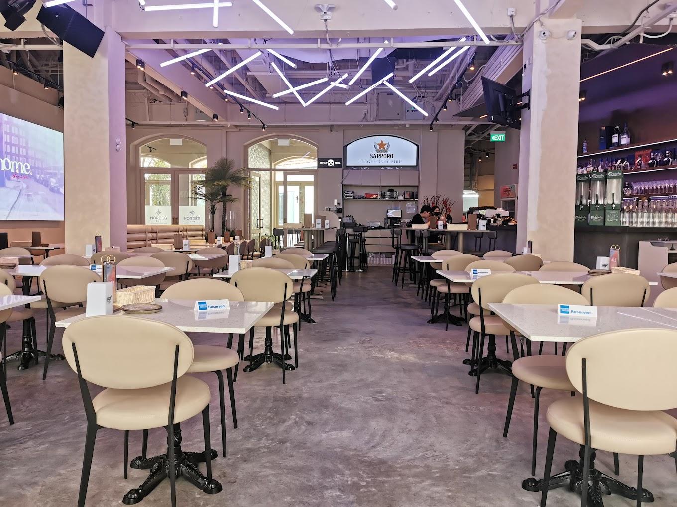 An event space with marble tables, cream chairs, illuminated ceiling lights, and a backlit bar at HOME Dawn & Dusk.