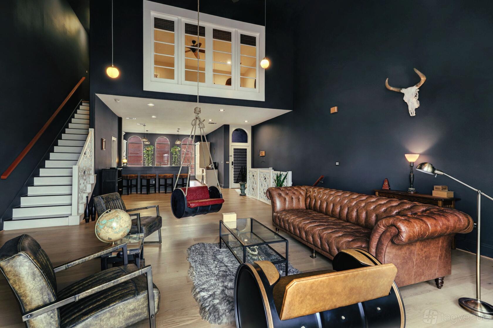 An apartment lounge with dark walls, a brown leather sofa, glass coffee table, and exposed staircase at Texas Gentleman's Lounge.