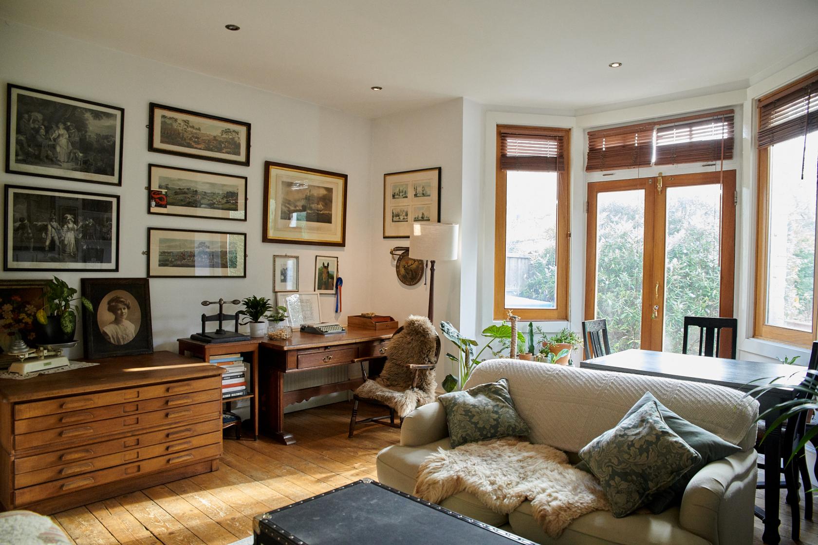 A photo studio with vintage furniture, framed art, wood floors, and large windows at Victorian Flat with overgrown garden.