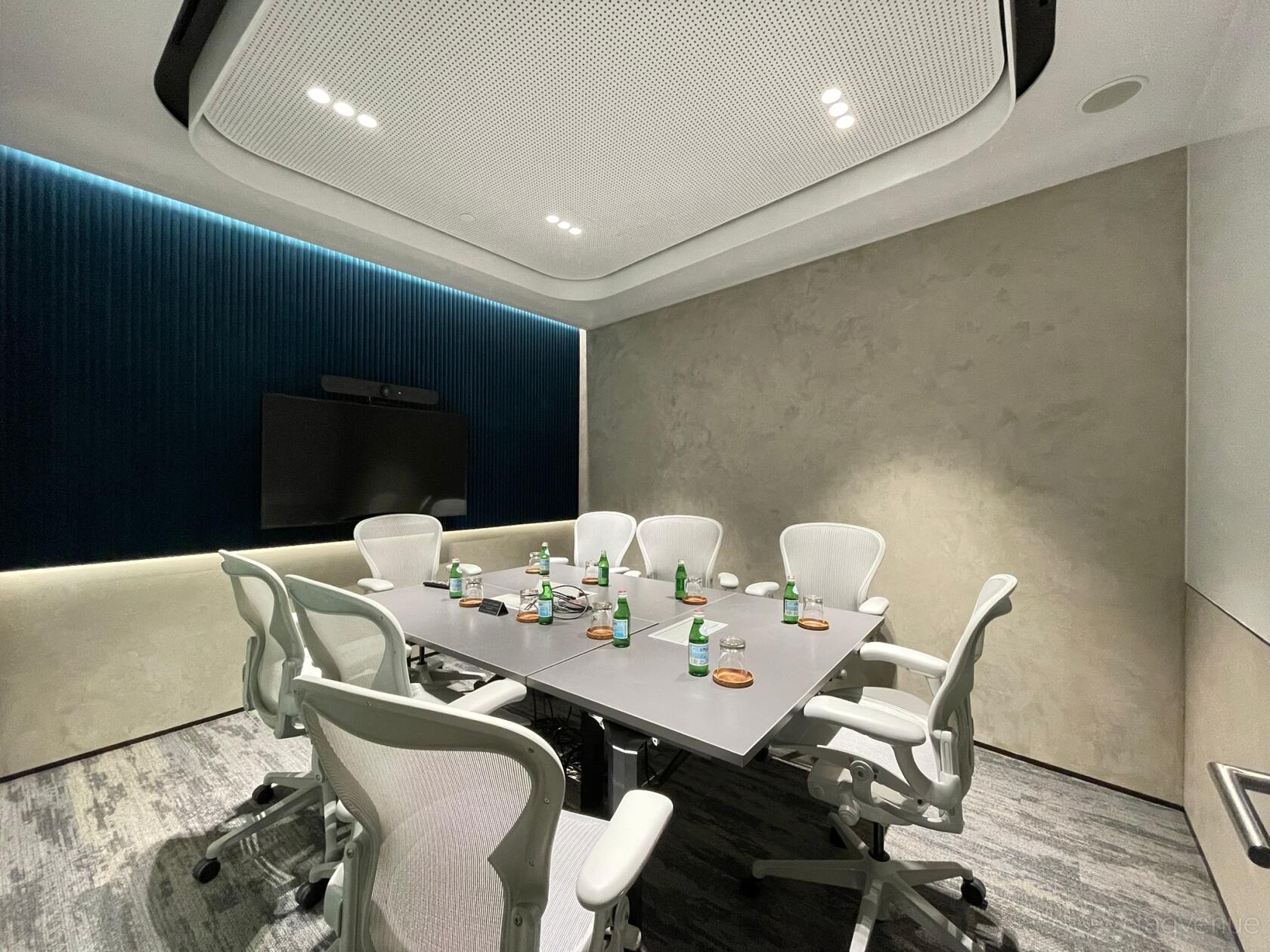 A meeting room with a rectangular table, ergonomic chairs, wall-mounted display, and textured blue accent wall at Capital Square.