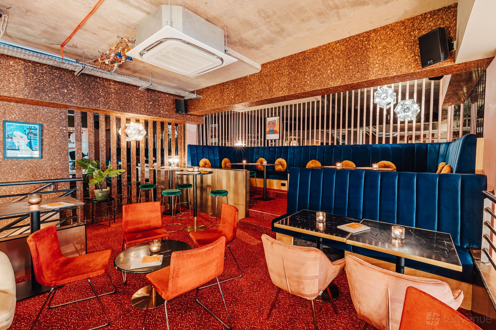 An event space in a cocktail bar with velvet booth seating, gold accents, and round tables on a red carpet at Someday.