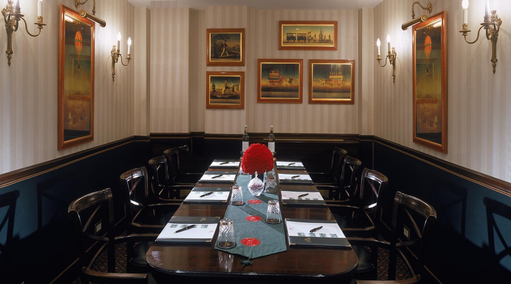 A hotel boardroom with a polished wood table, striped wallpaper, framed art, and wall sconces at The Chesterfield Mayfair.