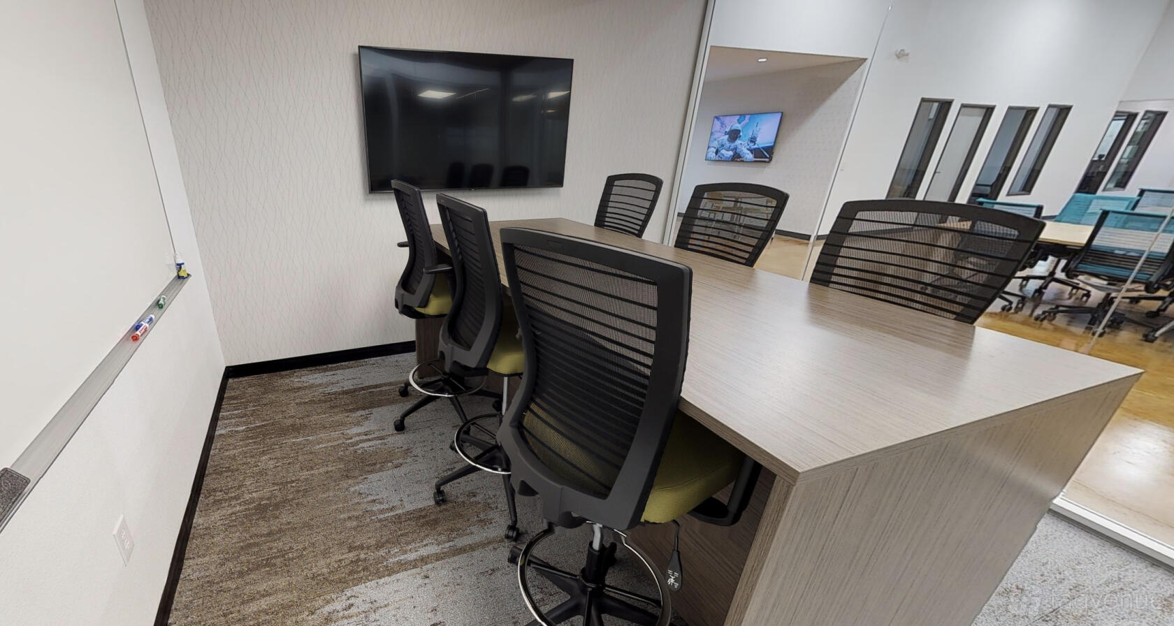 A coworking space with a large conference table, high-back chairs, wall-mounted TV, and whiteboard at Innovation WorkSpaces.