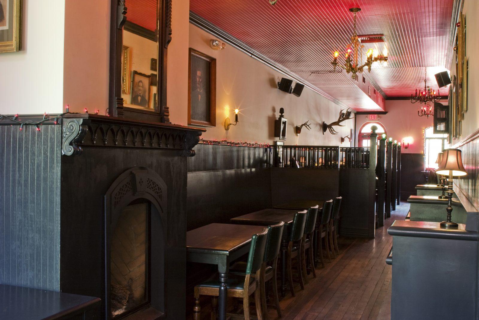 A bar with dark wood booths, framed portraits, wall sconces, and a decorative fireplace at Black Rabbit.