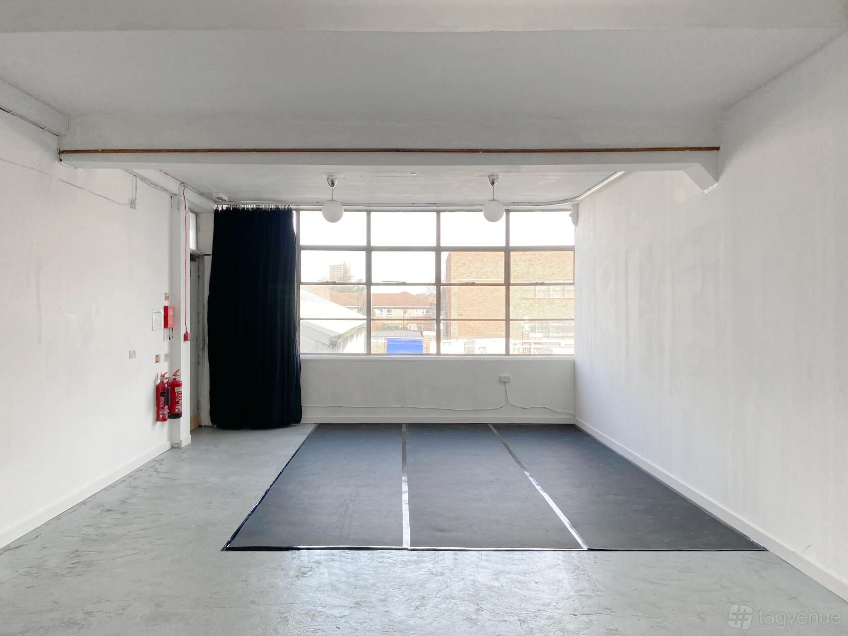 A blank canvas studio with white walls, gray floors, large industrial windows, and black floor mats at London Performance Studios.