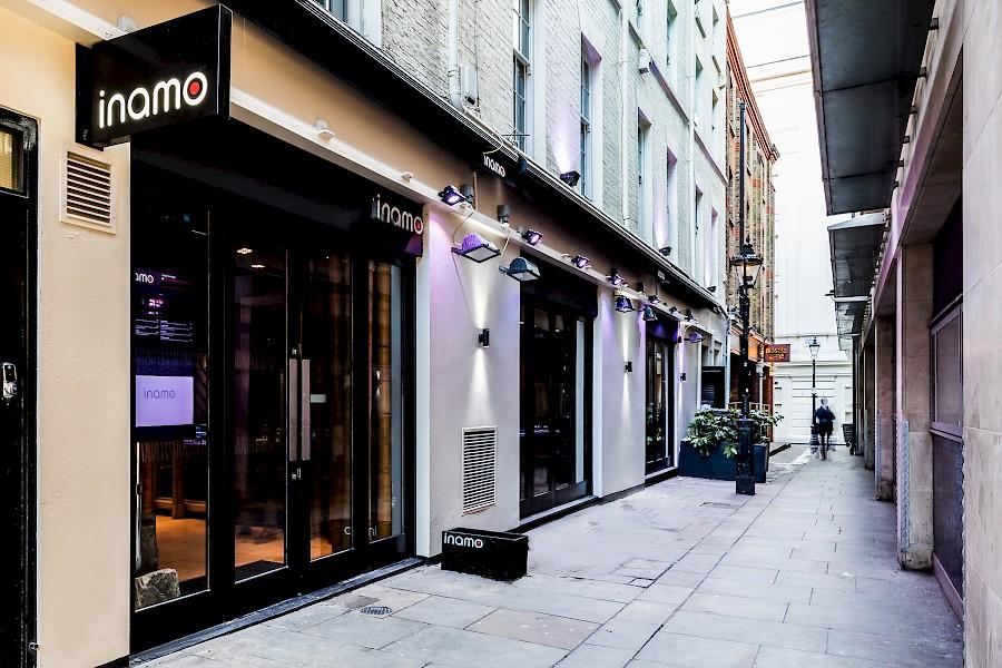 A restaurant exterior with glass windows, black awning, and modern lighting at Inamo Covent Garden.