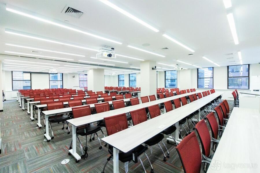 An auditorium with rows of red chairs, long white tables, and floor-to-ceiling windows at Midtown East Jay Suites.