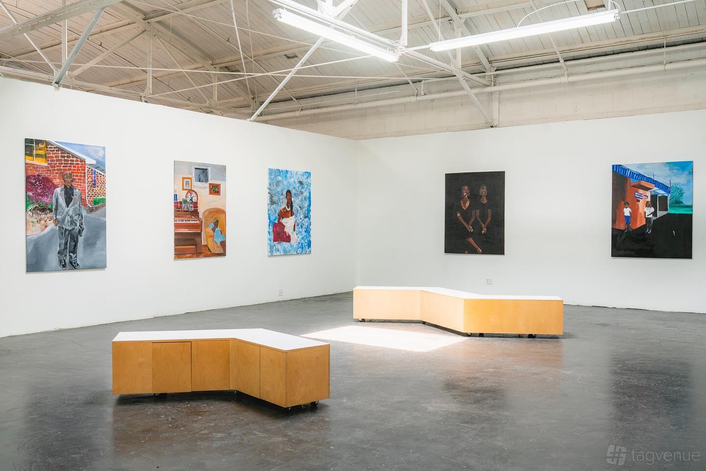 A gallery in a warehouse with white walls, exposed ceilings, modern benches, and contemporary artwork at Sanman Studios.