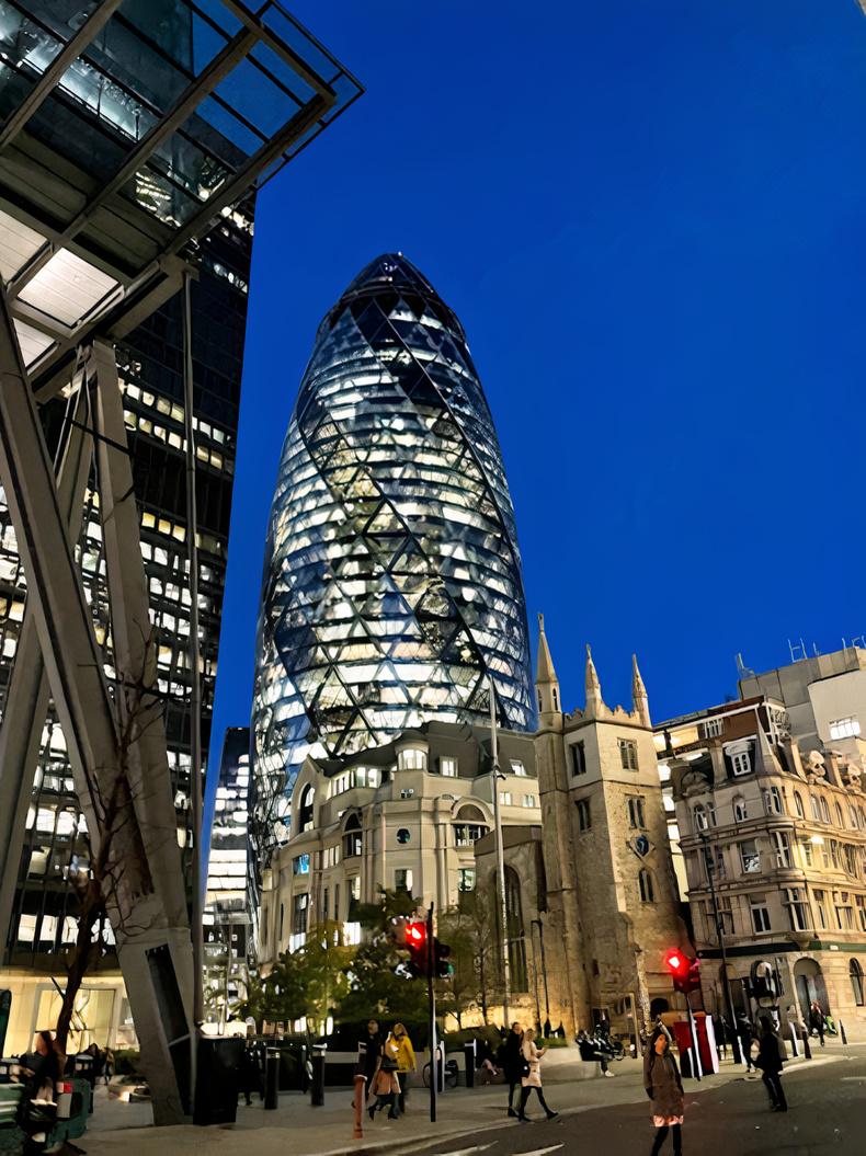 A landmark glass skyscraper with a distinctive curved shape illuminated at night at Searcys at The Gherkin.