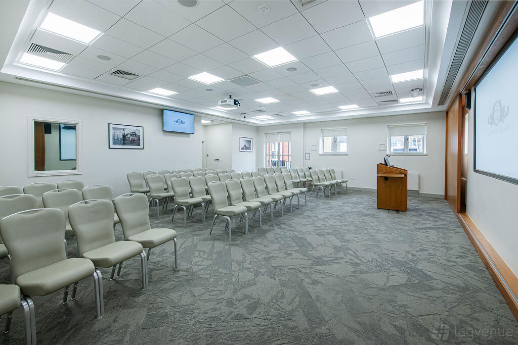 A meeting room with rows of beige chairs, a podium, and dual projection screens at No.11 Cavendish Square.
