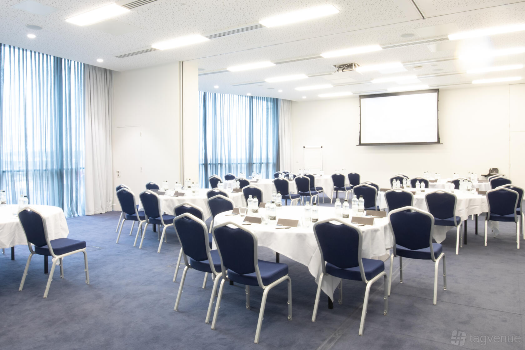 A meeting room with round tables, blue chairs, and floor-to-ceiling windows at Pullman Liverpool.