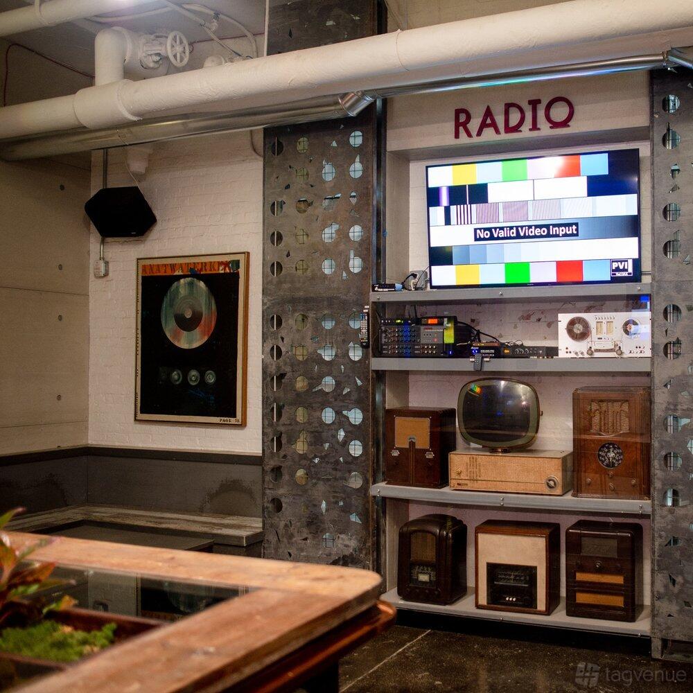 An event space with vintage radios, a wall-mounted TV, and industrial metal panels at RPM Underground.