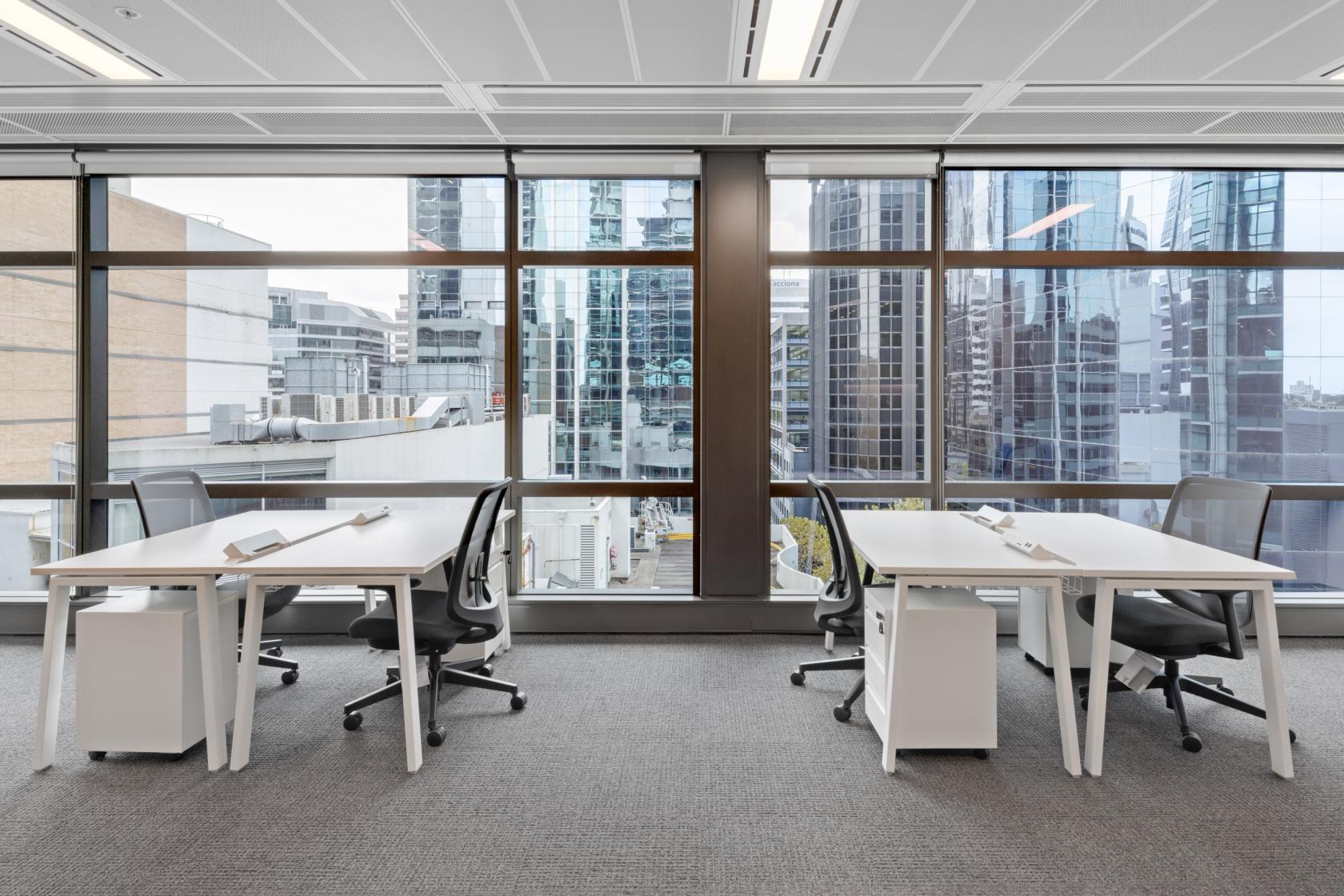 An office space with floor-to-ceiling windows, skyline views, and desks with ergonomic chairs at The Work Project at 100 Arthur Street.