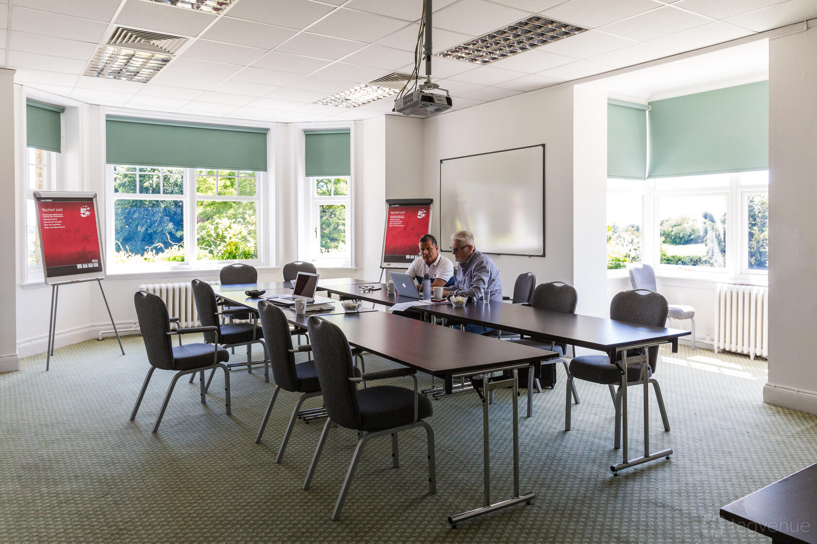 A meeting room with large windows, green carpet, modular tables, and flip charts at Middle Aston House.