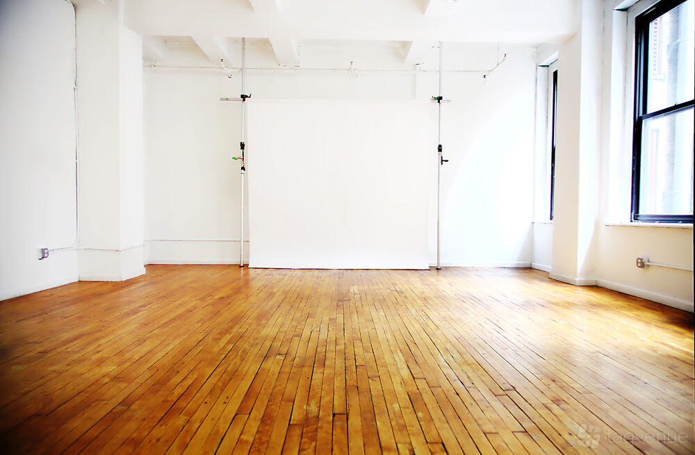 A photo studio with hardwood floors, white walls, a backdrop, and large windows at FAIRWAY STUDIOS.