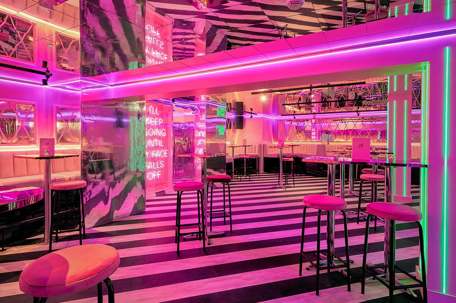 A cocktail bar with neon lighting, high tables with pink stools, and striped flooring at Tonight Josephine Birmingham.