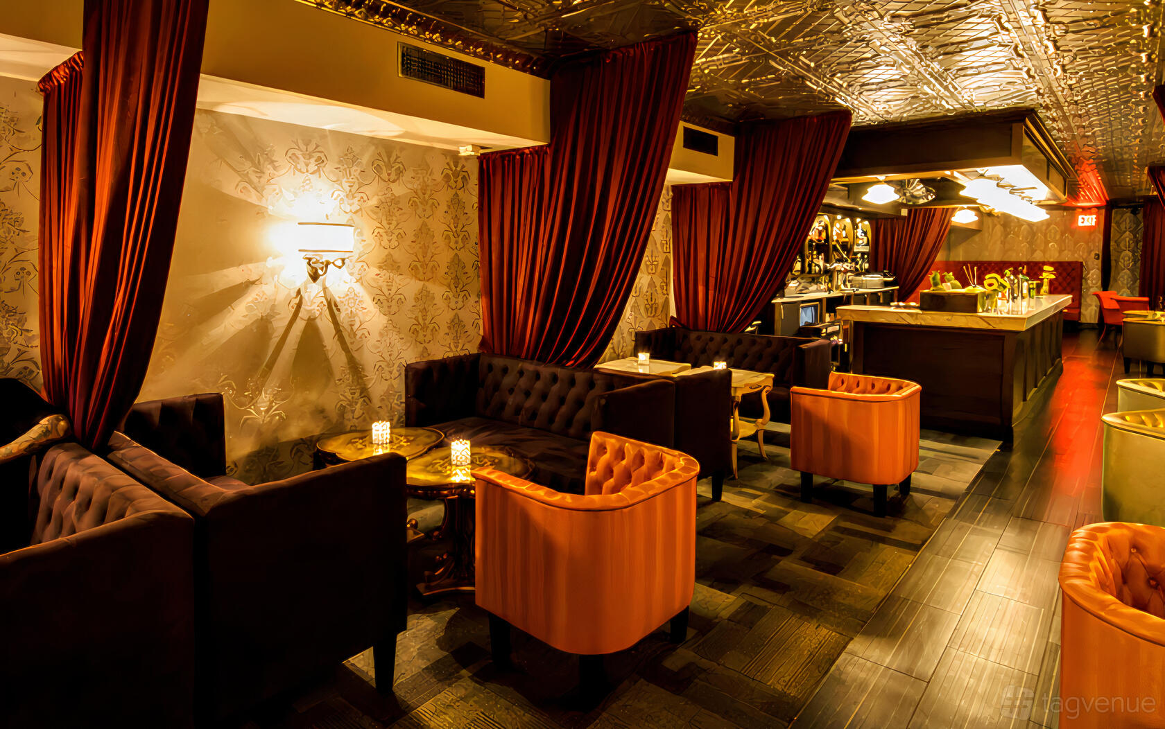 A cocktail lounge with tufted sofas, velvet drapes, patterned wallpaper, and a marble-topped bar at The Last Word.