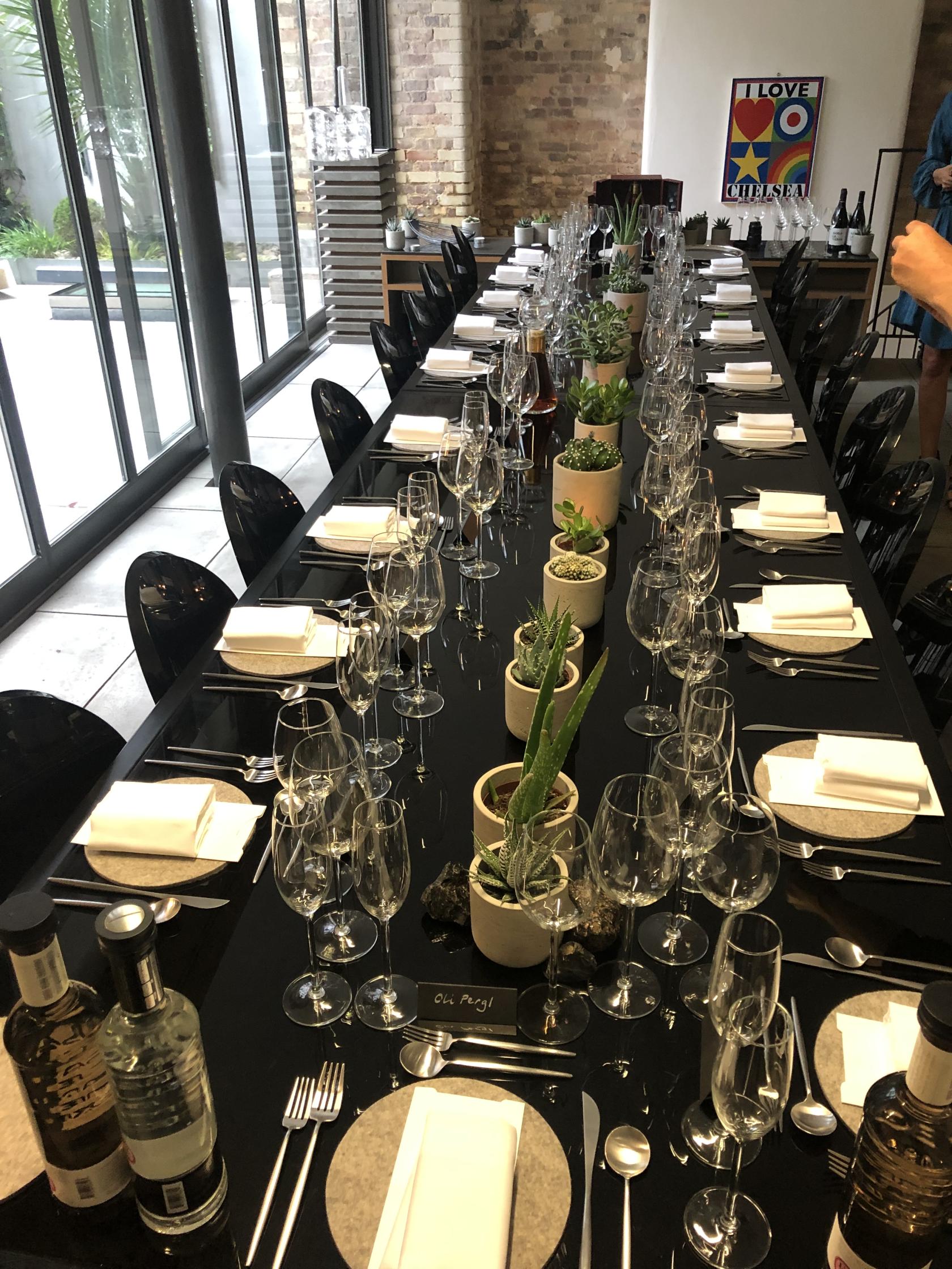 A warehouse dining area with a long black table, black chairs, and potted succulents at Sizona Location.