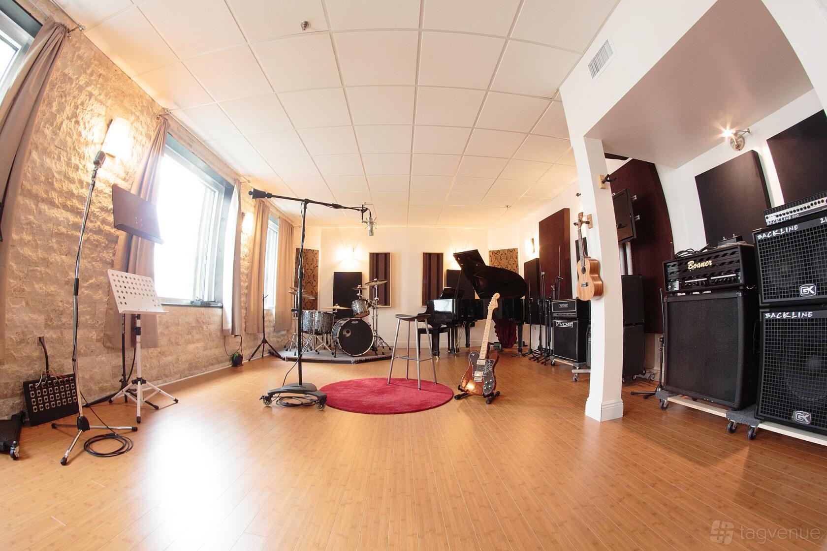 A recording studio with a drum kit, grand piano, guitars, amplifiers, and natural light at Heiga Studios.