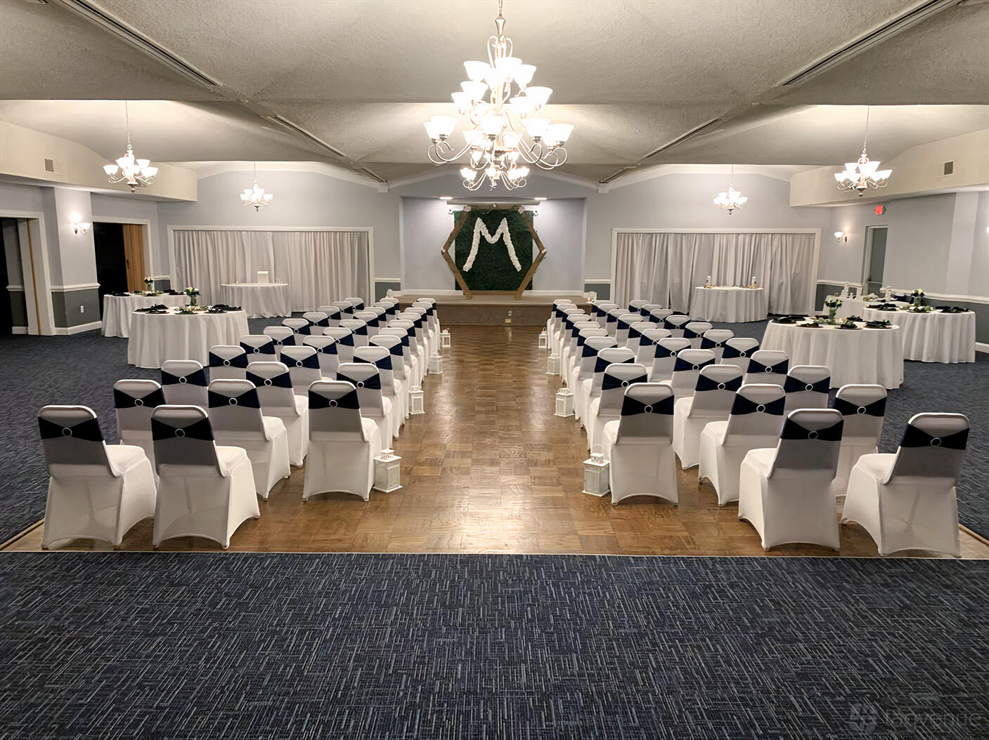 A ballroom with rows of chairs covered in white linen facing a parquet dance floor and stage at Rosensteel Hall.