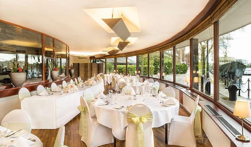 A restaurant in a hotel with large curved windows, round tables with white linens, and wood floors at Copthorne Hotel Manchester.