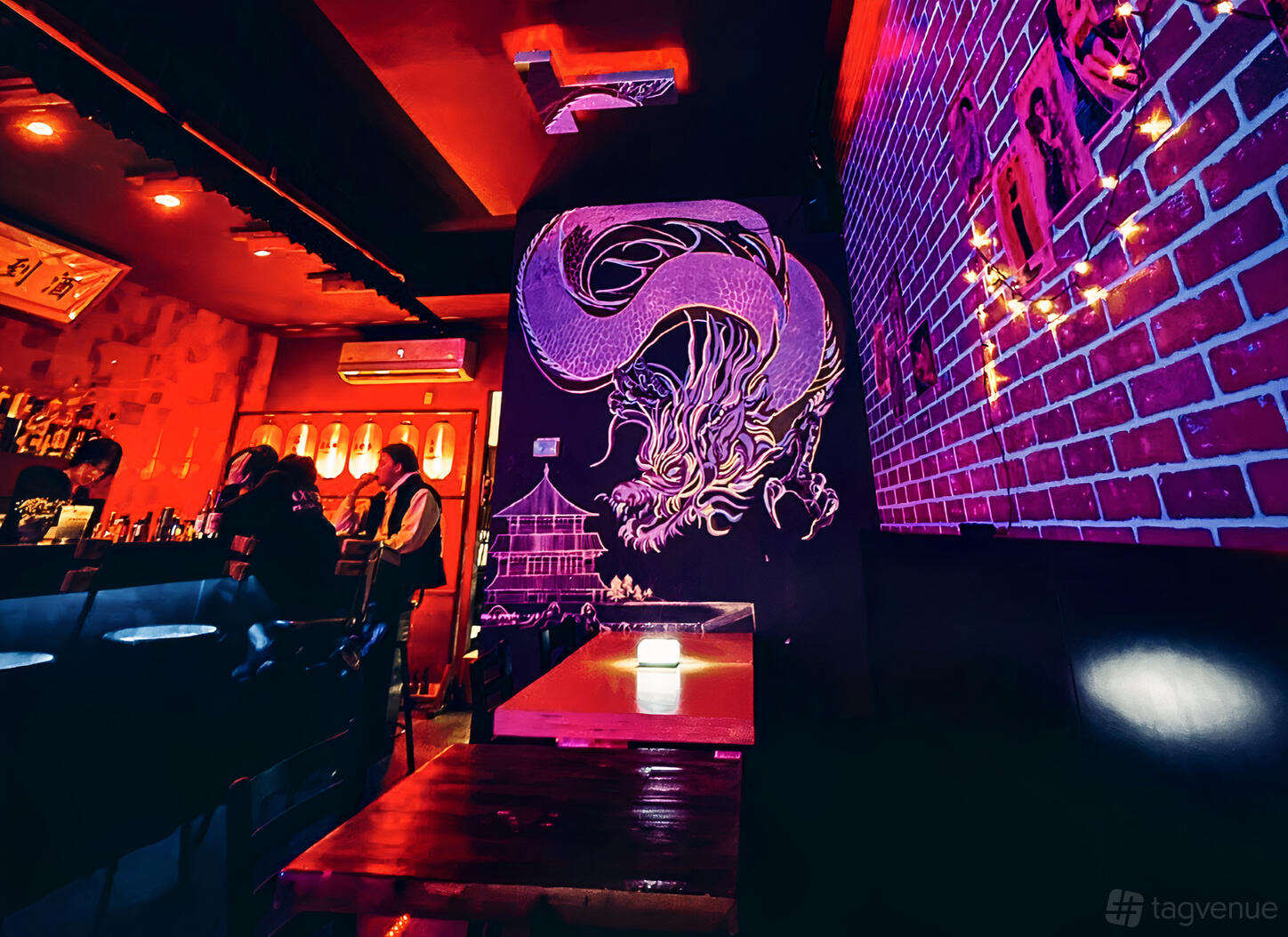 A bar with red lighting, exposed brick walls, dragon mural, and string lights at OnOff Toronto.