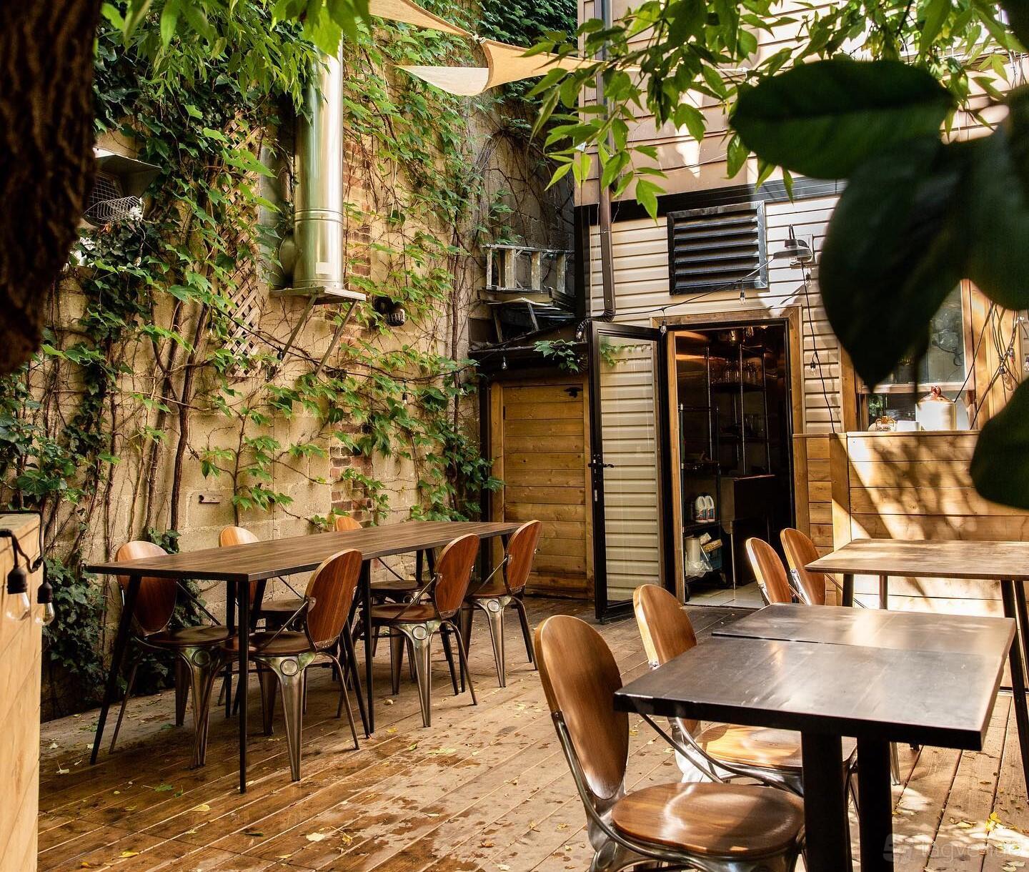 An outdoor restaurant space with wooden tables, metal chairs, and leafy vines along the walls at Hawker.