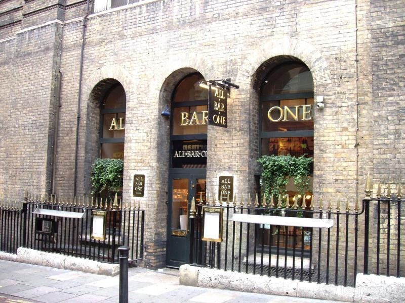 A pub with arched windows, brick facade, gold signage, and iron railings at All Bar One Charing Cross.